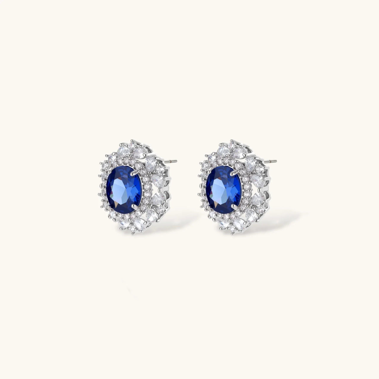 White gold plated jewelry set with blue cubic zirconia centers surrounded by clear crystal halos on cream background.