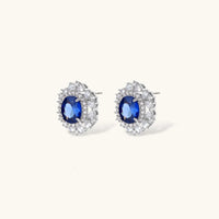 White gold plated jewelry set with blue cubic zirconia centers surrounded by clear crystal halos on cream background.