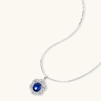 White gold plated jewelry set with blue cubic zirconia centers surrounded by clear crystal halos on cream background.