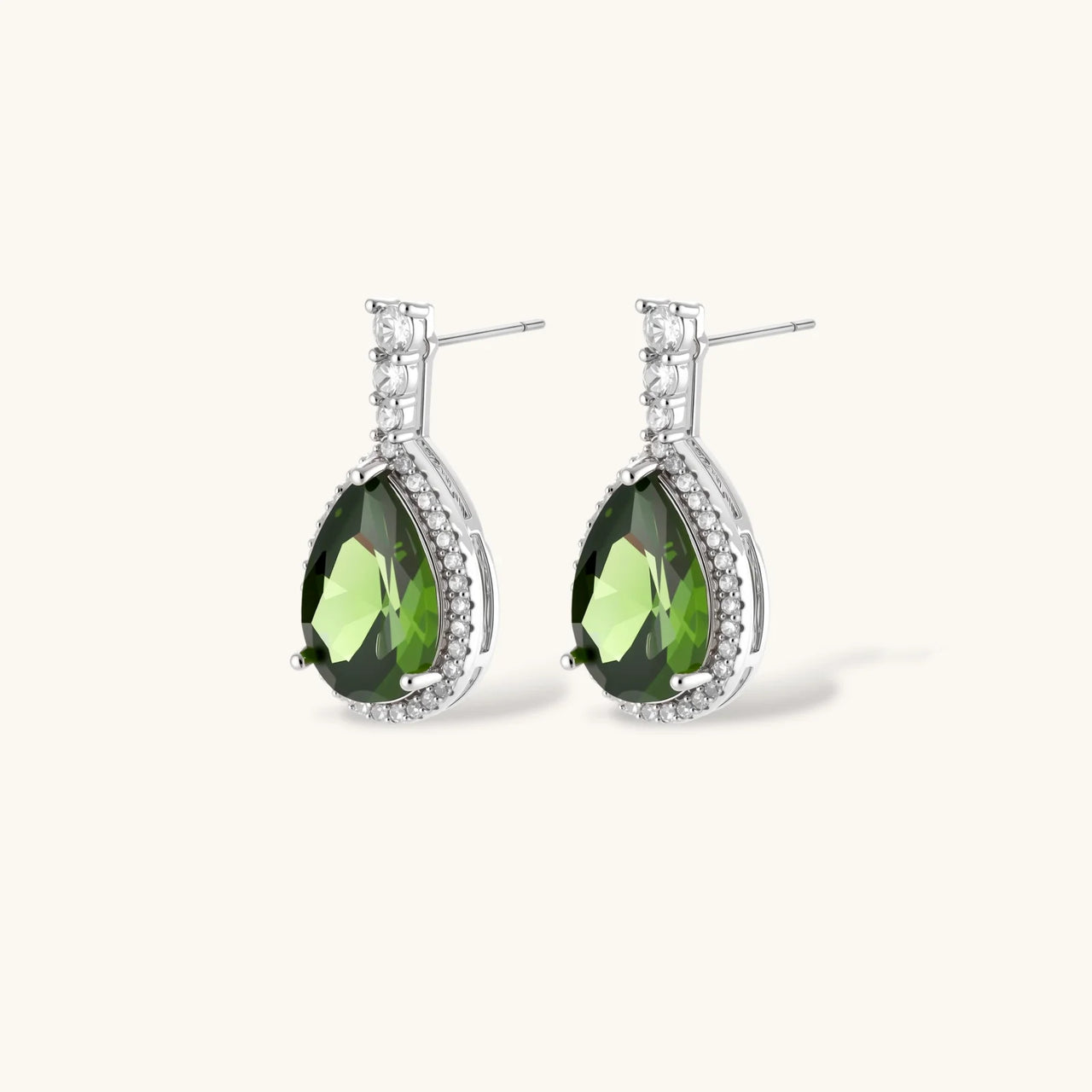 White gold plated jewelry set with green teardrop gemstones and cubic zirconia halos on cream background.
