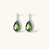 White gold plated jewelry set with green teardrop gemstones and cubic zirconia halos on cream background.