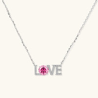 Sterling silver LOVE necklace with pink moissanite stone replacing the O, featuring crystal-set letters on delicate chain.