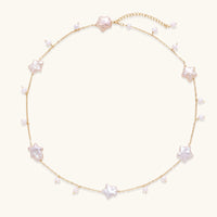 Gold vermeil chain with iridescent star-shaped baroque pearls and small round freshwater pearl drops on cream background.