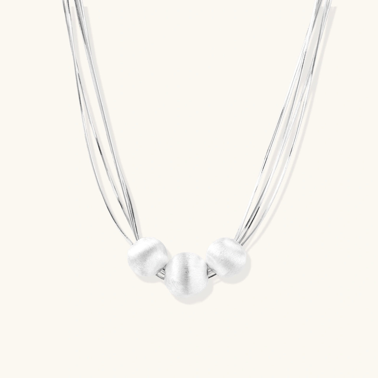 Sterling silver multi-strand necklace with three brushed round beads on cream background