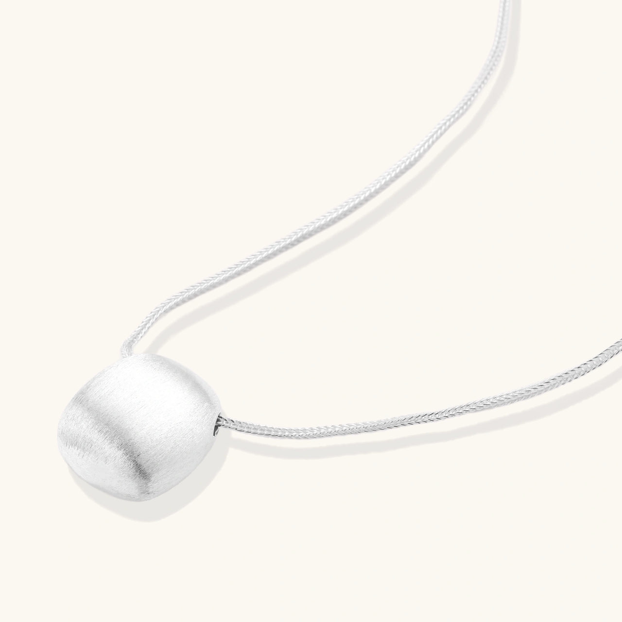 Minimalist brushed sterling silver dome pendant on delicate chain against cream background, showing matte textured finish