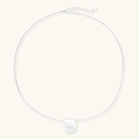 Minimalist brushed sterling silver dome pendant on delicate chain against cream background, showing matte textured finish