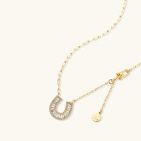 Gold-plated horseshoe necklace and earring set with baguette and round crystals arranged in geometric pattern on white background.
