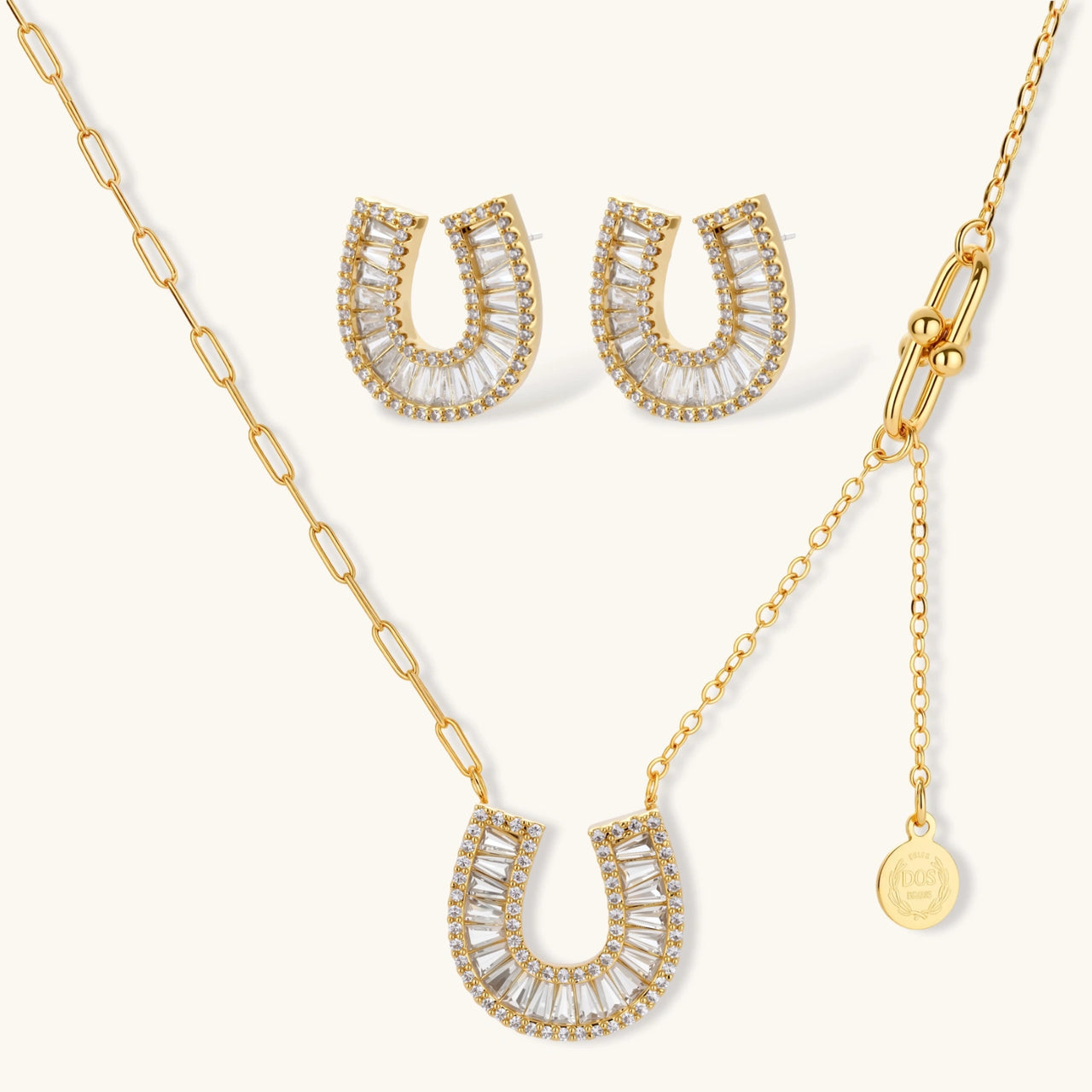 Gold-plated horseshoe necklace and earring set with baguette and round crystals arranged in geometric pattern on white background.