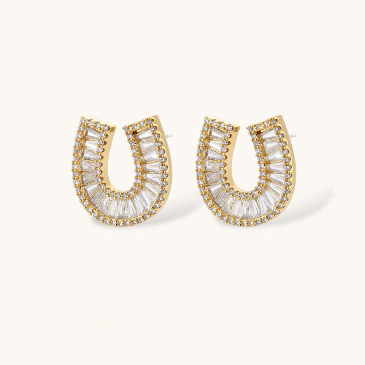 Gold-plated horseshoe necklace and earring set with baguette and round crystals arranged in geometric pattern on white background.
