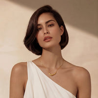 A model wearing a Curve Statement Necklace, featuring a sleek curved gold-plated pendant against a neutral background.