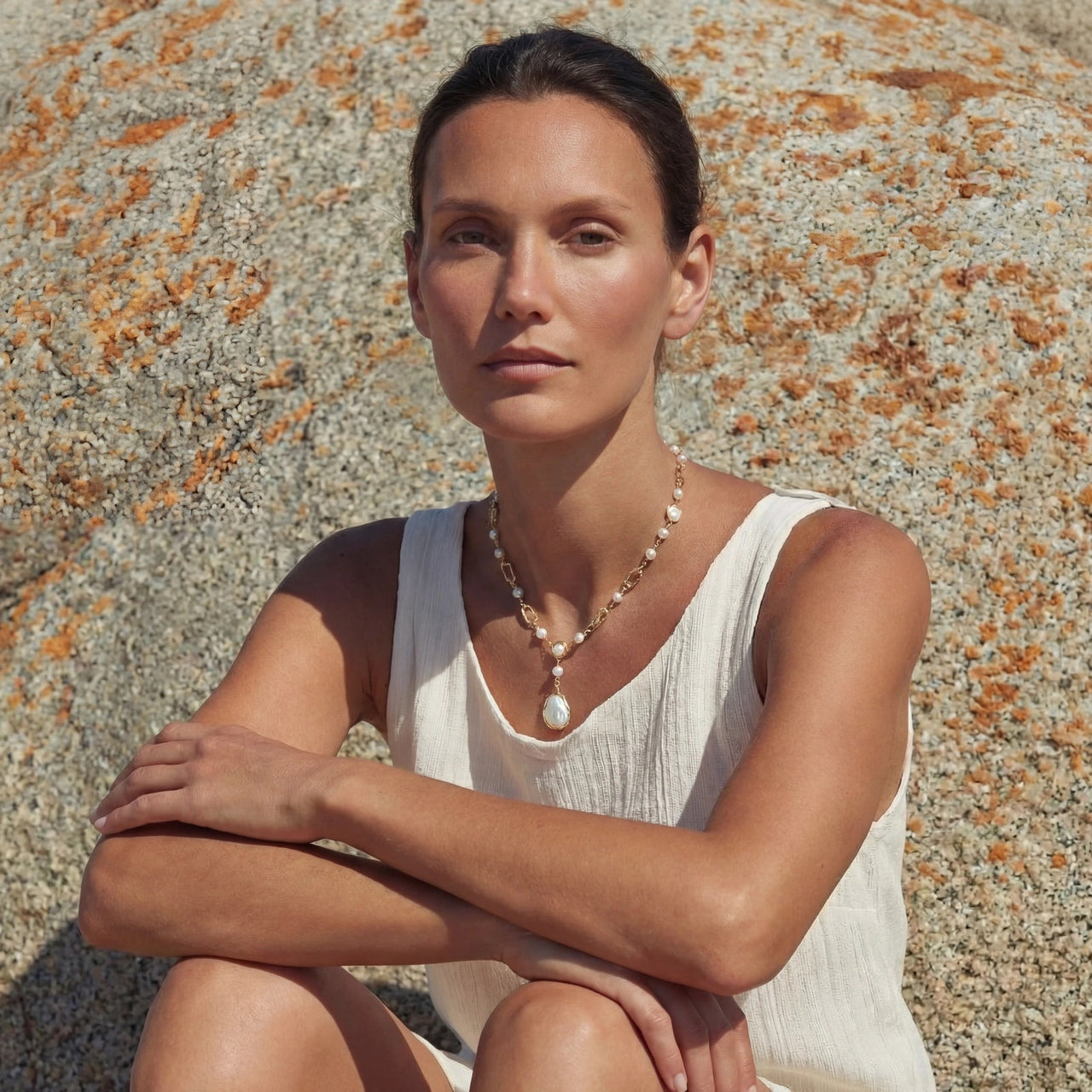Woman wearing Lumina Pearl Station Necklace, surrounded by nature and rocks, showcasing elegant freshwater pearls.
