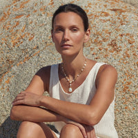 Woman wearing Lumina Pearl Station Necklace, surrounded by nature and rocks, showcasing elegant freshwater pearls.